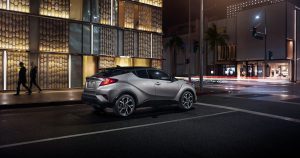 A 2019 Toyota C-HR stopped at a busy downtown intersection at night.
