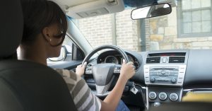 A teen driver sitting in the drivers seat of a new car.